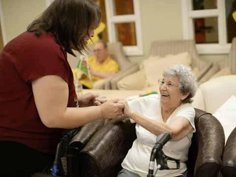 A caregiver helping an elderly woman in a care-home lounge